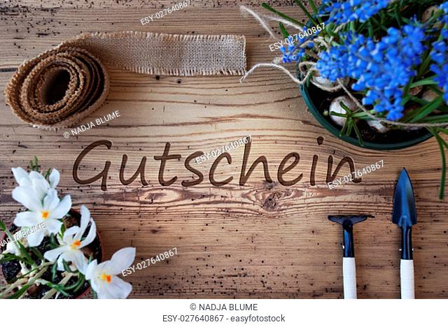 German Text Gutschein Means Voucher. Spring Flowers Like Grape Hyacinth And Crocus. Gardening Tools Like Rake And Shovel. Hemp Fabric Ribbon