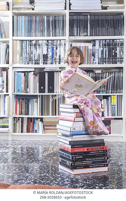 Happy little girl seated on top of a pile of books