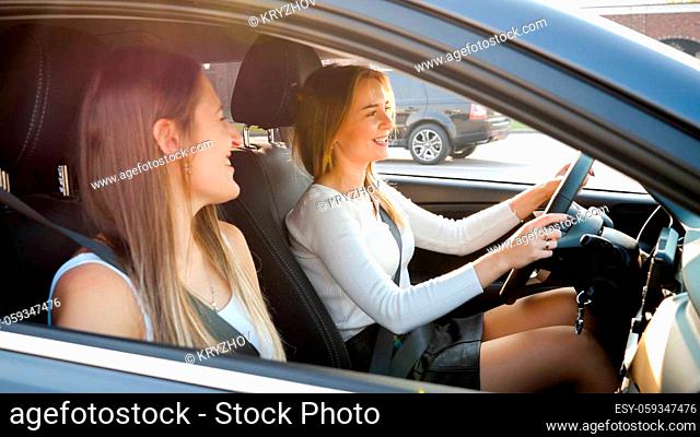 Portrait of two girls talking and smiling while driving in car with open windows