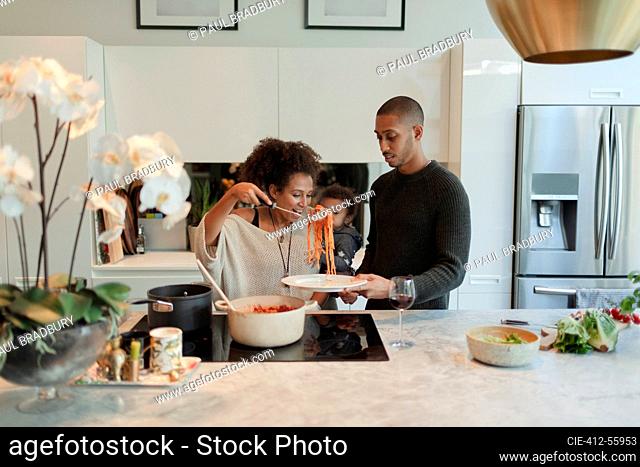 Couple with baby daughter cooking spaghetti in kitchen