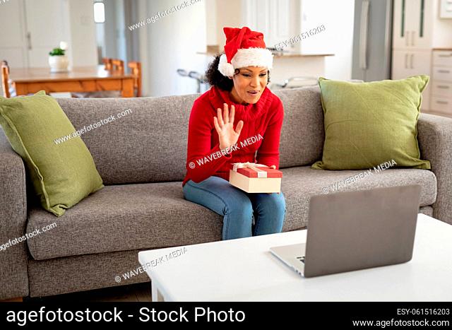 Woman in Santa hat holding gift box while having a video chat on laptop at home
