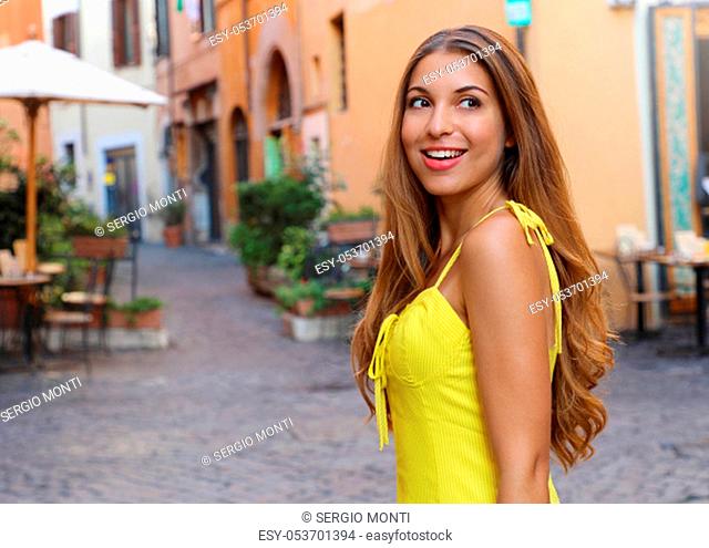 Elegant portrait of beautiful fashion woman with long hair in yellow summer dress walking in Trastevere neighborhood Rome, Italy