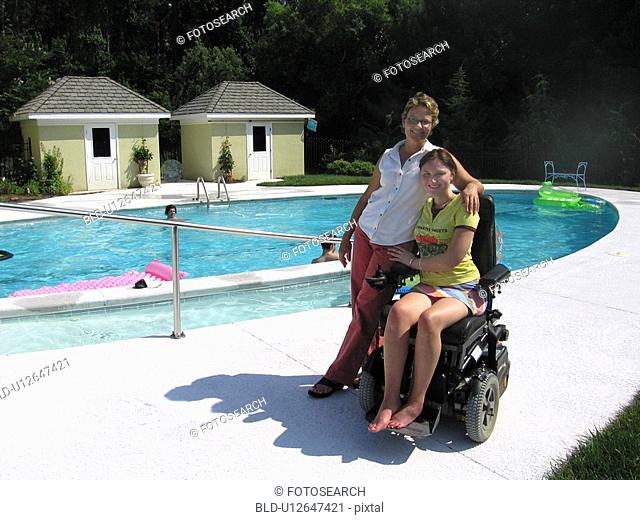 Mother and daughter (electric wheelchair user) relax by the accessible entrance to their pool