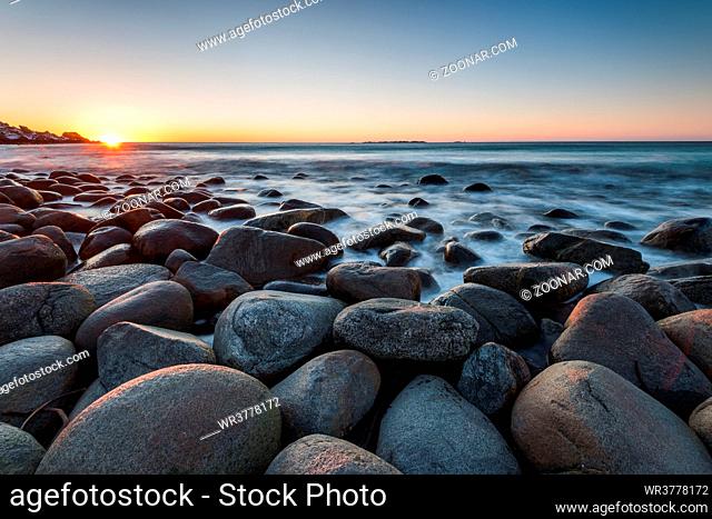 The famous beach near Uttakleiv with round shaped rock boulders on the Lofoten islands in Norway on clear winter day with snow-clad mountains and blue sky after...