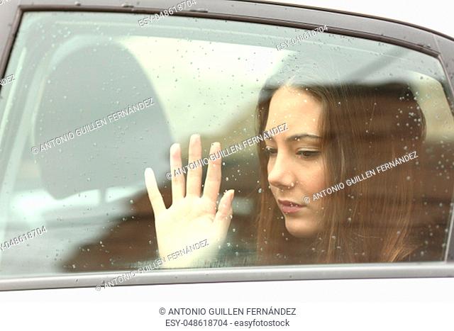 Sad woman touching window inside a car during a roadtrip a rainy day