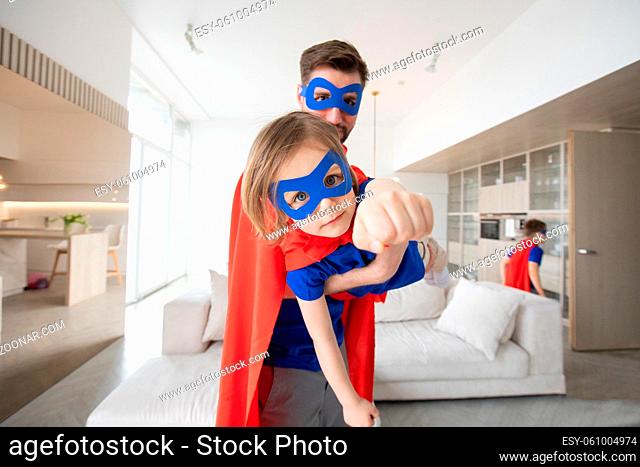 Father holding son flying in superhero costume at home