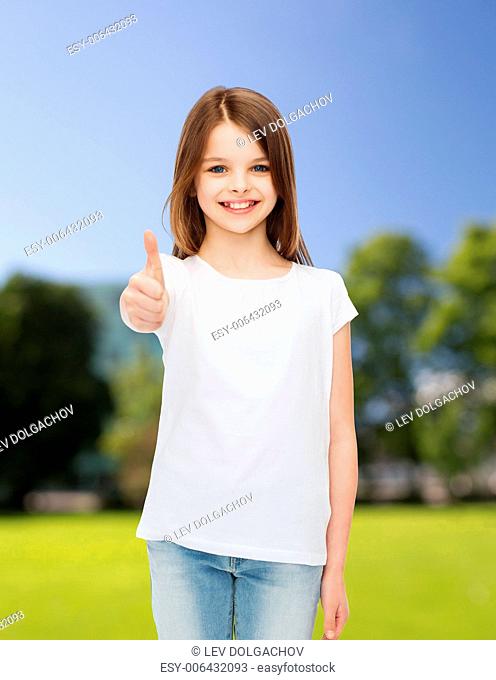 advertising, childhood, nature and people - smiling little girl in white blank t-shirt showing thumbs up gesture over green park background