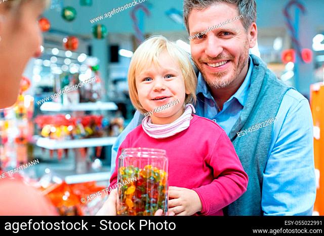 Child girl grabbing some sweets out of a jar in the candy store