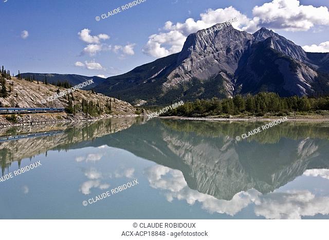 Athabasca River reflecting mountains and a passenger train travelling through the Rocky Mountains in Jasper National Park, Alberta, Canada