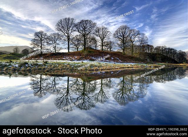 UK - England Cumbria Near Ullswater View along the River Brathay on a sunny winter's day showing reflections of the sky and distant fells and two people walking...