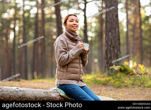 asian woman with mug drinking tea in forest
