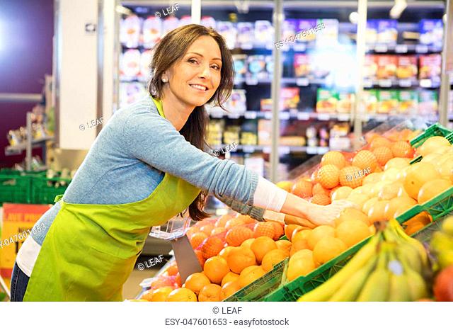 Portrait of smiling saleswoman arranging oranges in supermarket