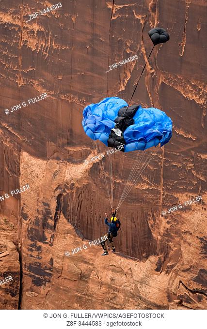 A BASE jumper free-falls from the clifftop 950 vertical feet above the valley floor at Mineral Canyon near Moab, Utah. His pilot chute has deployed and extracts...