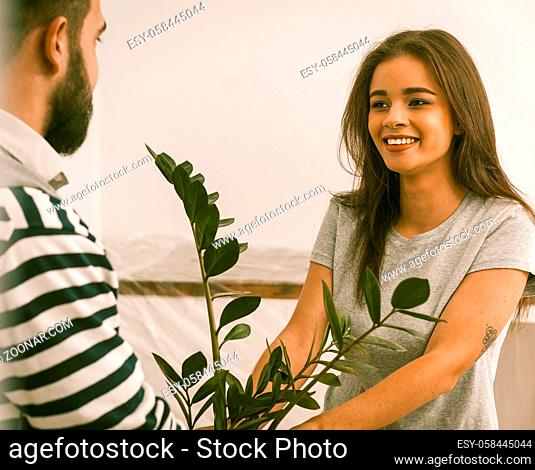 Close Up Portrait Of Happy Young Couple Relocated To New Flat, Man And Woman Smiling Holding Plant In Their Hands, Toned Image
