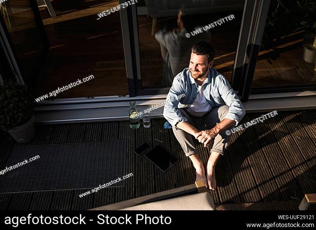 Thoughtful freelancer sitting with hands clasped on porch