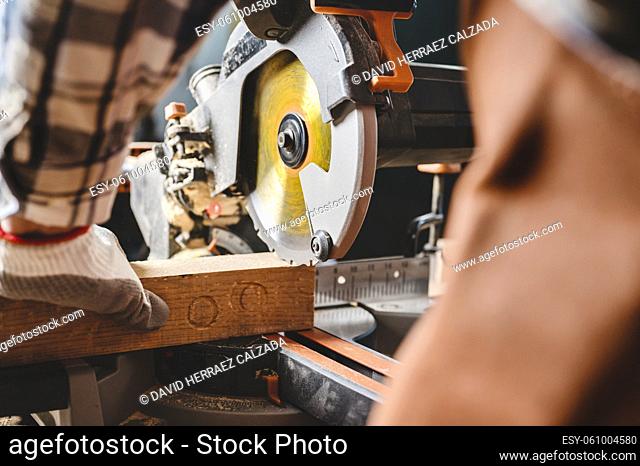 Carpenter is sawing a wood plank with electric circular saw machine in carpentry workshop. Workwood DIY concept. High quality photography