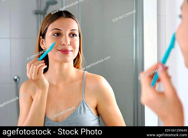 Beautiful young woman shaving her face by razor at home. Pretty woman using razor on bathroom