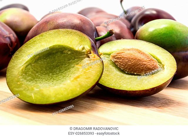 Juicy plum cuted in half on wooden board. Group of plums visible. Isolated on white background