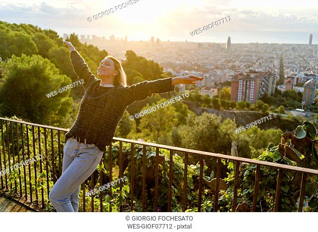 Carefree young woman standing above the city at sunrise, Barcelona, Spain