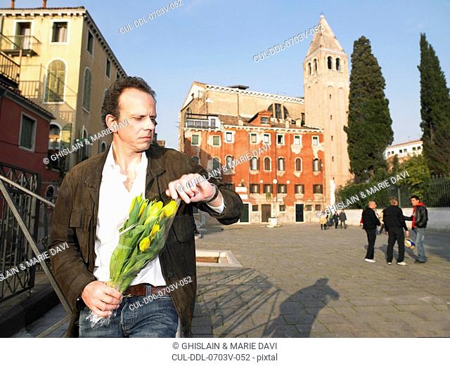 Man waiting with bunch of tulips, looking at his watch Venice, Italy