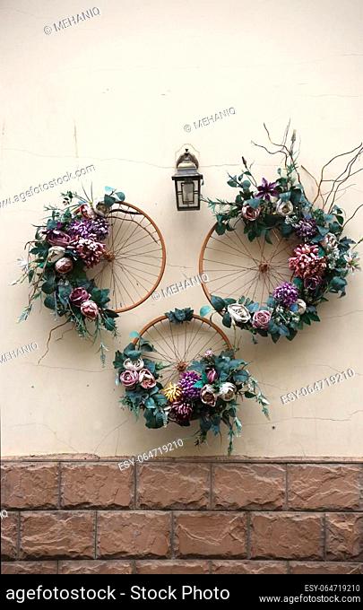 Decoration urban art object from bicycle wheels and colorful elegant flowers on wall