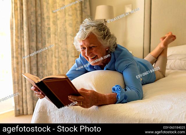 Senior caucasian woman lying in bed and reading book in bedroom