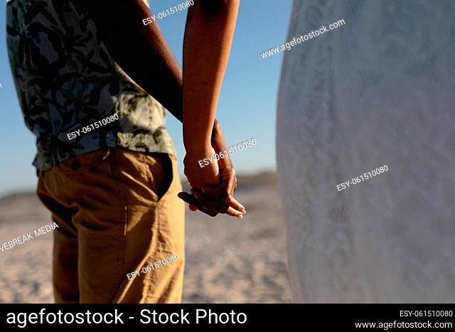 Mixed race couple holding hands and smiling into the camera on a sunny day