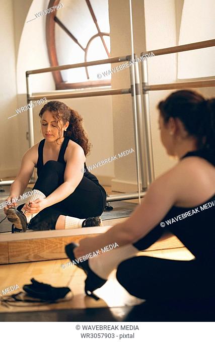 Irish dancer sitting front of mirror on floor tying her shoelace