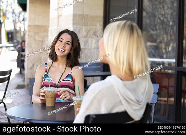 Two woman sitting outside at a cafe drinking coffee and talking