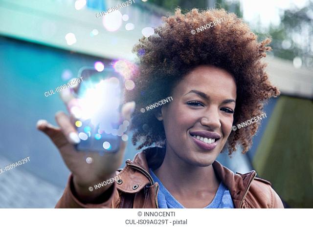 Young woman holding up smartphone with glowing lights coming out