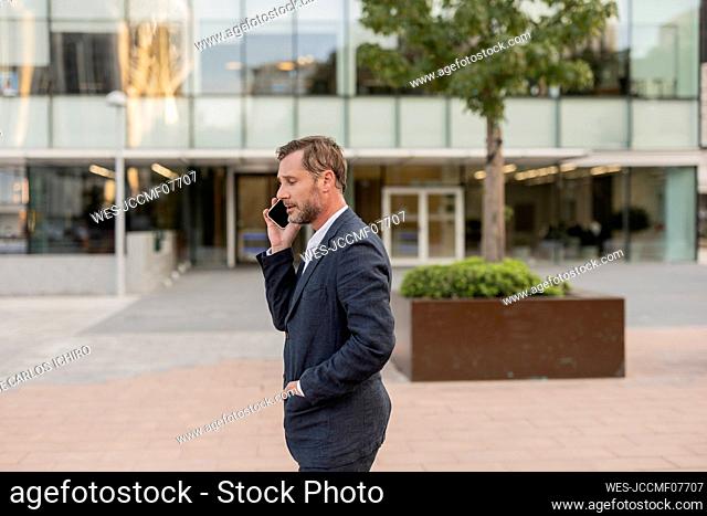 Businessman talking through smart phone outside office building