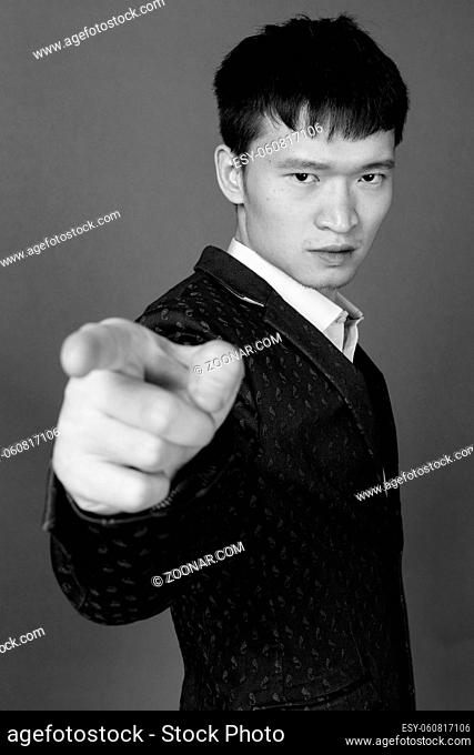 Studio shot of young Chinese businessman against gray background in black and white
