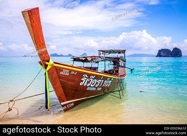 Longtail boat in crystal clear blue waters waiting for passengers on beautiful white beach in Ko Mok, Thailand
