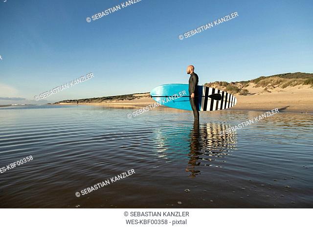 Spain, Andalusia, Tarifa, man holding stand up paddle board in the sea