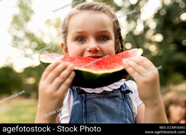 Cute girl eating watermelon standing at park