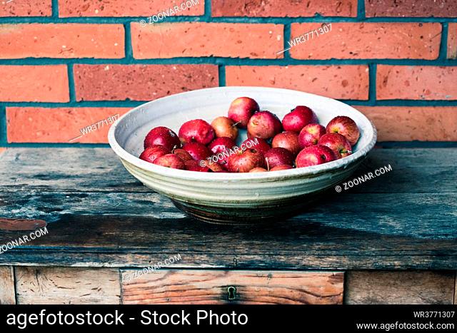 Closeup of big bowl of fresh red apples sprinkled raindrops on wooden table