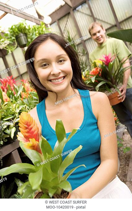 Young couple holding carrying potted plant in greenhouse portrait