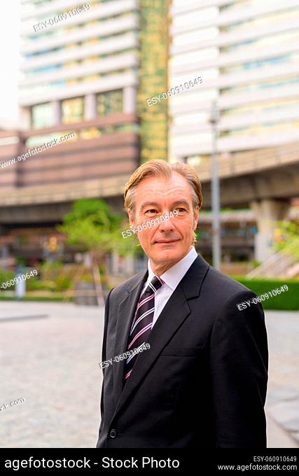 Portrait of mature handsome businessman wearing suit in the city streets outdoors