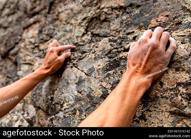 Closeup perspective on a rock climber ascending a limestone cliff in nature. White chalk covering hands and fingers to dry sweat and increase friction
