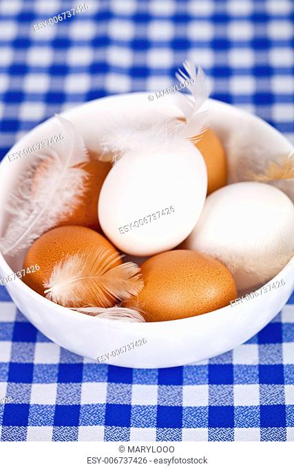 brown and white eggs, feathers in a bowl on tablecloth background