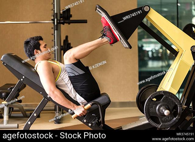 Full length side view of a fit and strong young man exercising at the leg press machine during lower body workout routine at the gym