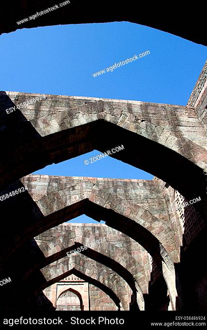 Low angle view of stone arches of Hindola Mahal or Swinging Palace audience hall with sloping side walls against blue sky, Mandu, Madhya Pradesh, India, Asia