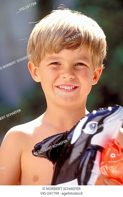 portrait, outdoor, blond 6-year-old boy with naked upper part of the body holding two swim animals  - GERMANY, 08/08/2004