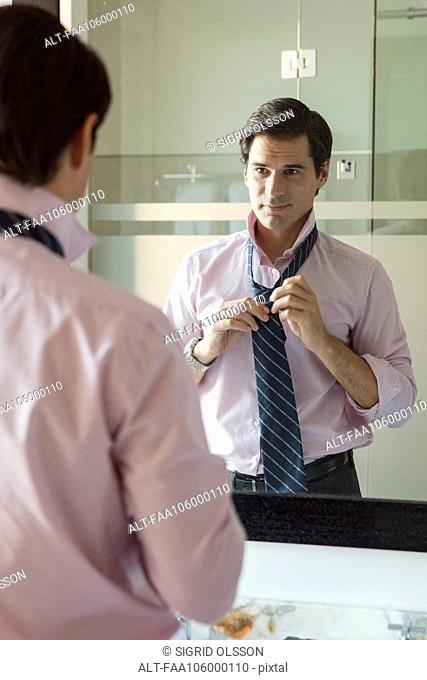 Man adjusting necktie in bathroom mirror