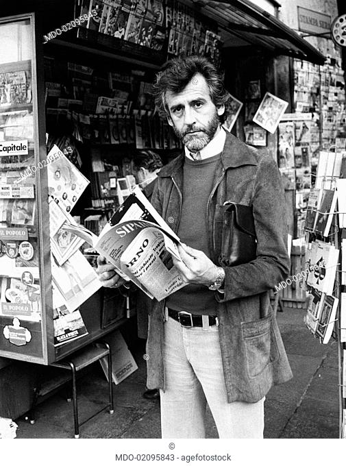 Italian actor Giulio Bosetti leafing through a magazine beside a newspaper kiosk. Turin, 1973