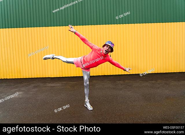 Man with arms outstretched balancing in front of yellow and green wall