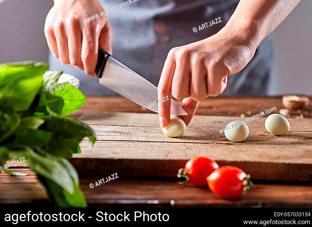 Boiled quail eggs cut female hands on a wooden board on a table with tomatoes and spinach. Step by step preparation