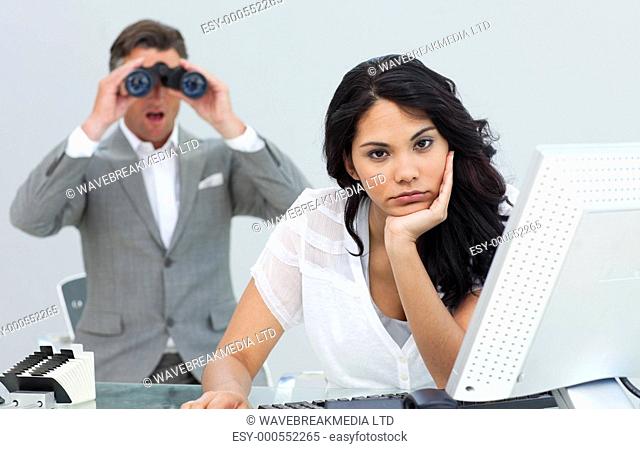 Brunette businesswoman annoyed by a man looking through binoculars in the office