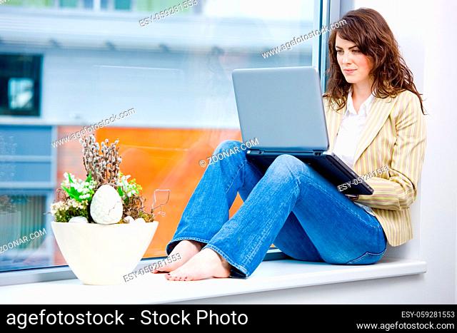 Young happy businesswoman sitting in office window and wokring on laptop computer, smiling