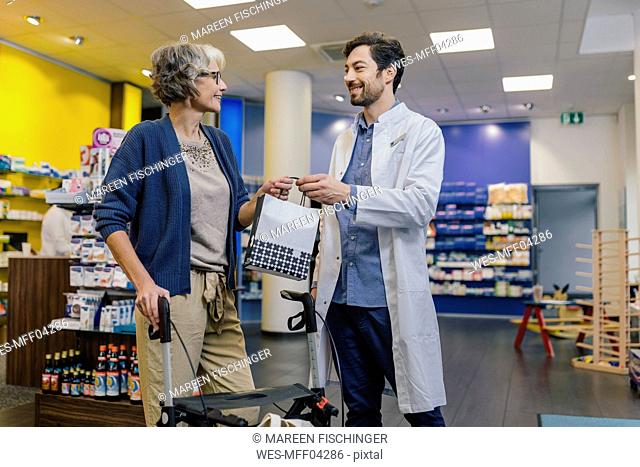 Pharmacist giving bag of medicine to customer with wheeled walker in pharmacy